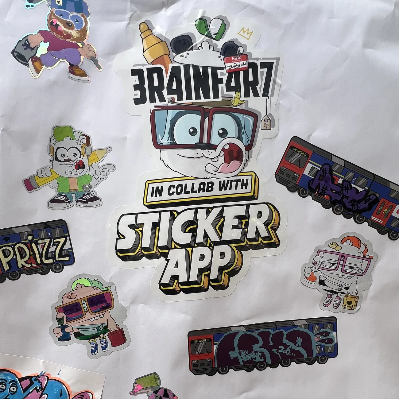 Seinä täynnä käsin väritettyjä Brainfart x StickerAppin muotoon leikattuja tarroja ja graffititägein koristeltuja S8 World -junaetikettejä