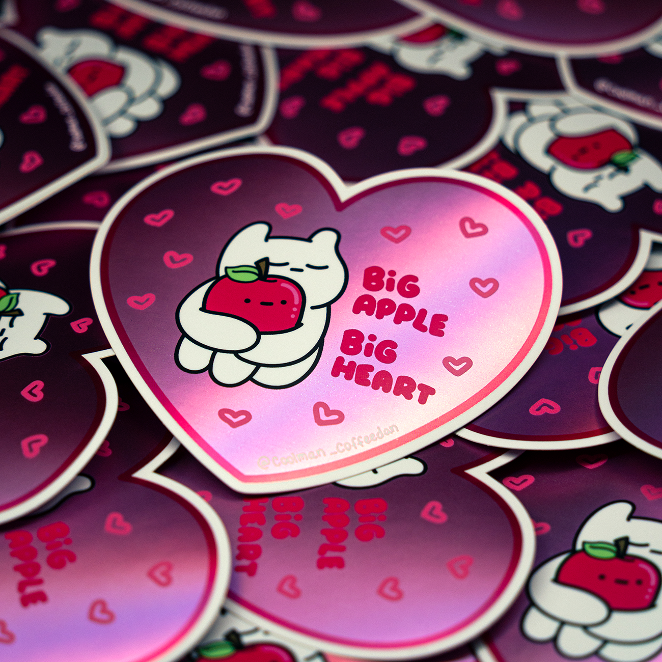 Heart-shaped stickers display a cartoon cat hugging an apple, with the text "Big Apple Big Heart" on a pink gradient background.