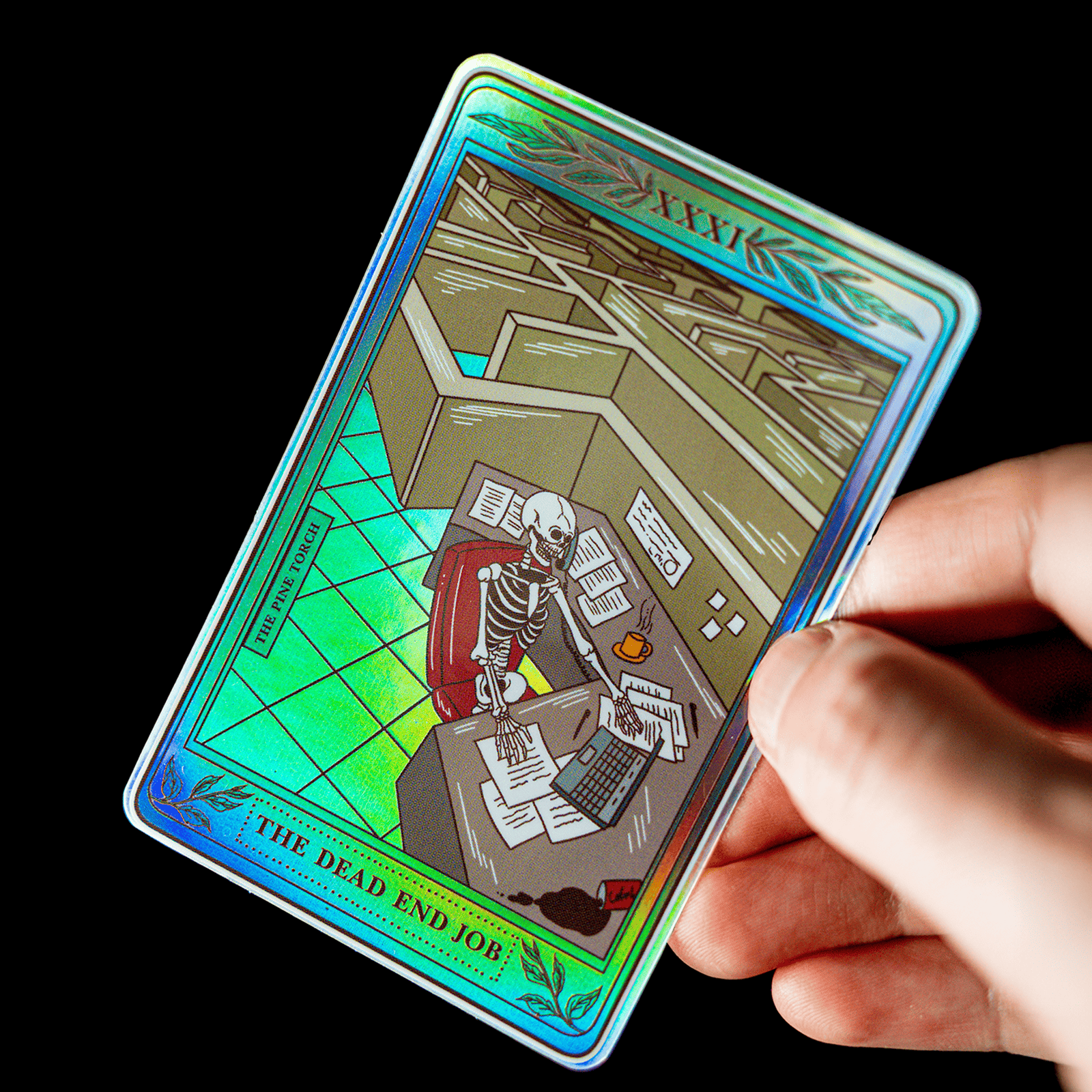 Käsi pitelee holografista tarot-kortin muotoista tarraa, jossa on otsikko ”The Dead End Job” ja luuranko toimistopöydän ääressä