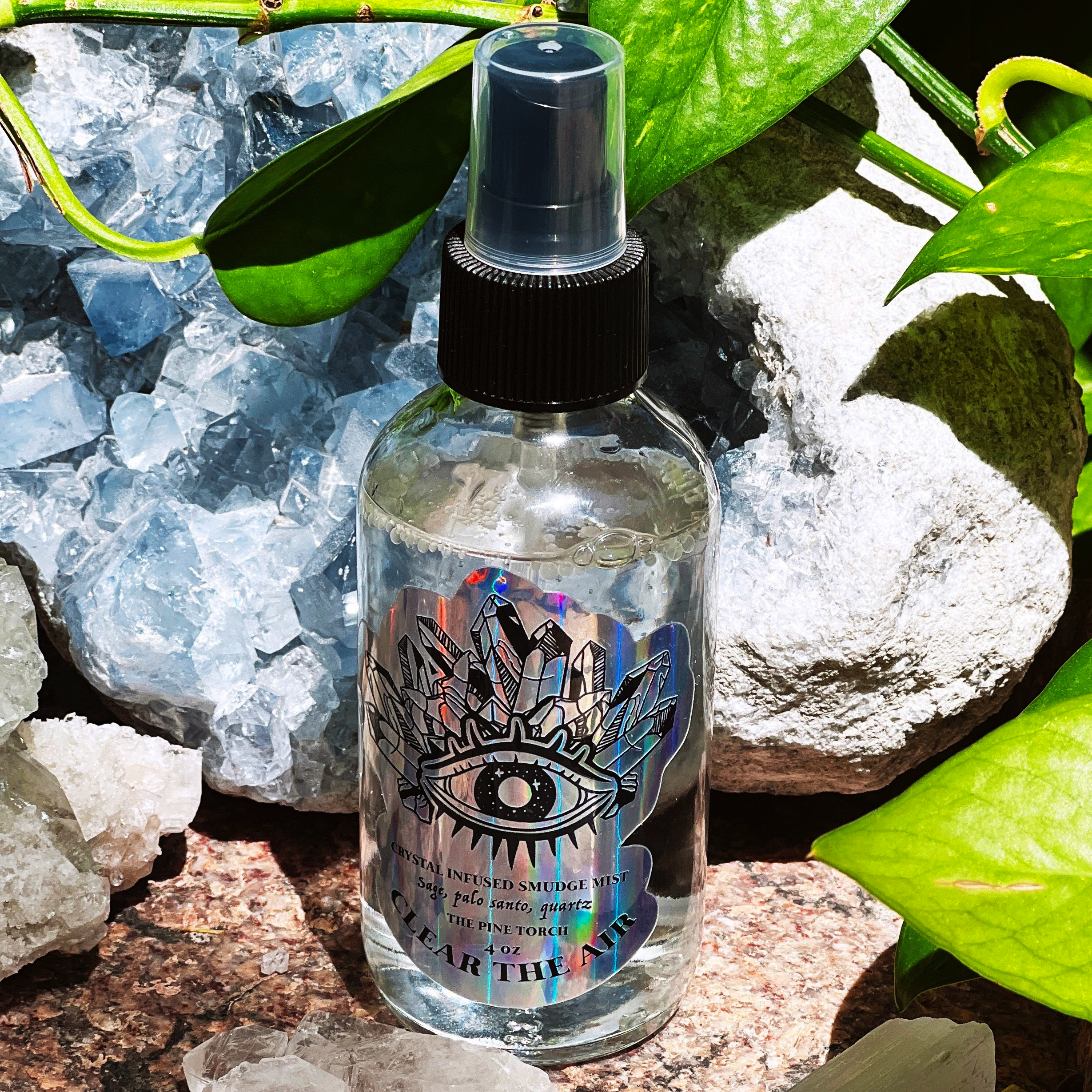 Spray bottle with a holographic die-cut sticker with the text "Clean The Air", standing on rocks and crystals