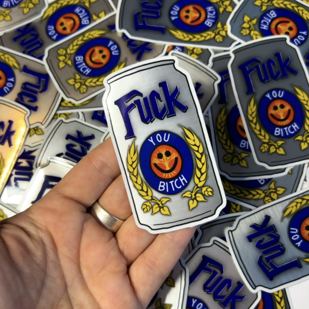 A person holding a brushed aluminum sticker of a can in front of a pile of stickers